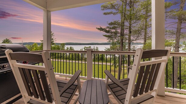 A covered outdoor seating area with a view of a lake and trees. - Luxe Lakefront Living on Stunning Crystal Lake in Benzonia, MI (Benzonia)