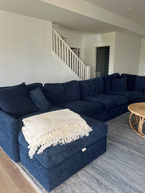 A dark blue sectional sofa with a white throw blanket, a wicker coffee table, and a patterned rug.