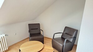 A small, modern room with a sloped ceiling, two leather chairs, a round wooden table, and a radiator on the floor. - City Apartment - Business, Uni, Handwerker - Free Wifi (Bochum)