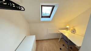 A small, well-lit room with a slanted ceiling, a desk with a lamp, a radiator, and a window. - City Apartment - Business, Uni, Handwerker - Free Wifi (Bochum)