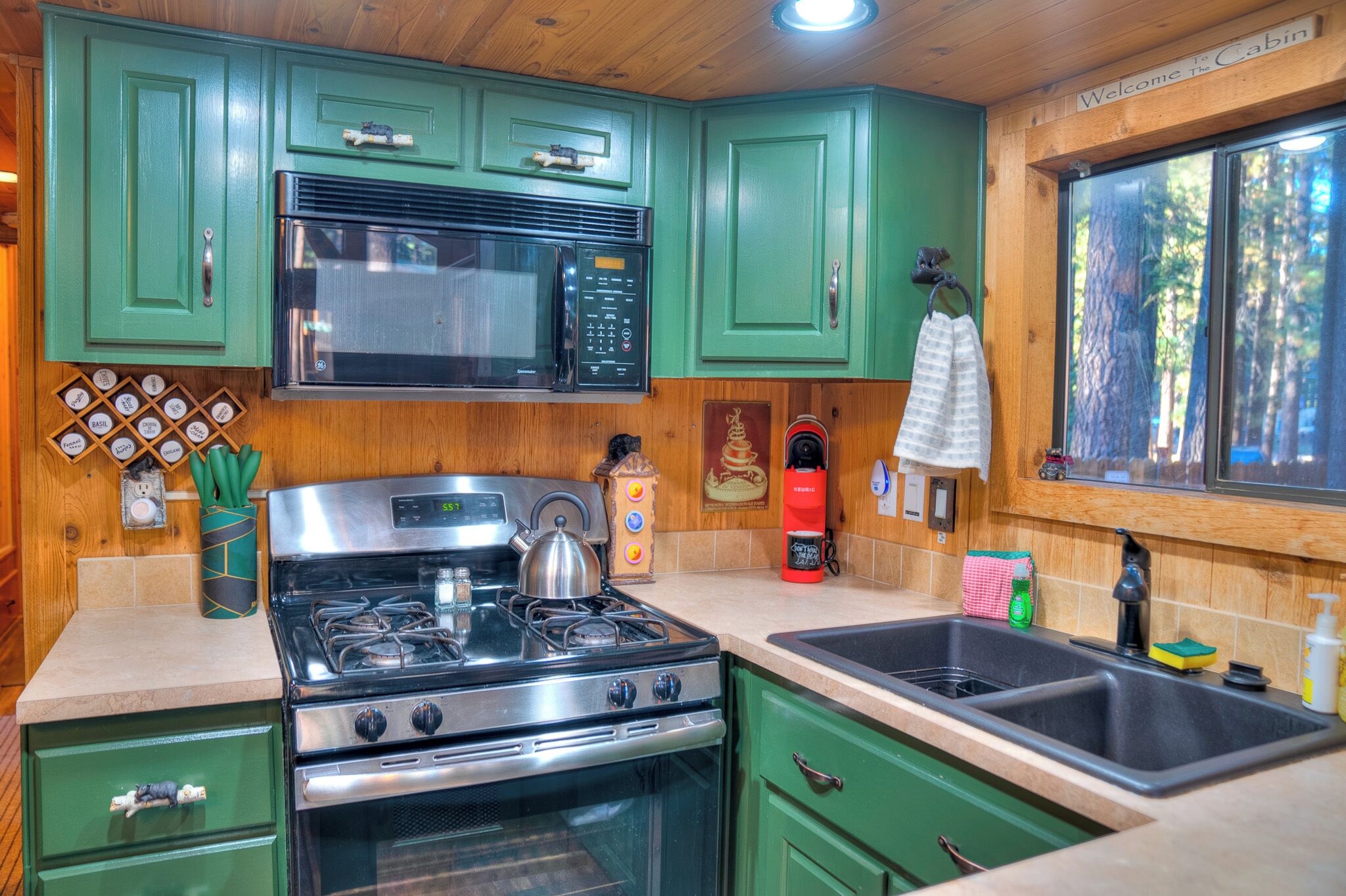 A kitchen with green cabinets, a stainless steel stove, a microwave, and a sink.
