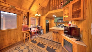Interior de una cabaña de madera con cocina, una mesa de comedor y una barra.