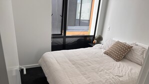 A neatly made bed with a striped comforter and a single patterned pillow, a bedside lamp, and a window with blinds.