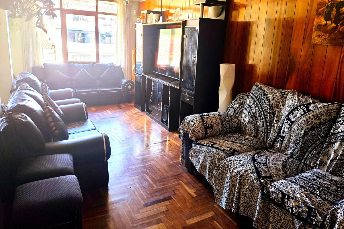 Una sala de estar con un sofá, un sillón estampado, un televisor y paneles de madera.