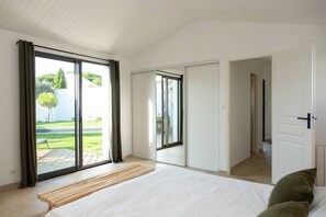 A bedroom with a large bed, sliding glass doors to a balcony, and a view of a green landscape. - Alma - Renovated villa with heated pool few blocks from the beach (LE BOIS PLAGE EN RE)