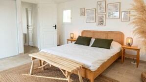 A bedroom with a wooden bed, two bedside tables with lamps, a bench, and framed artwork on the wall. - Alma - Renovated villa with heated pool few blocks from the beach (LE BOIS PLAGE EN RE)