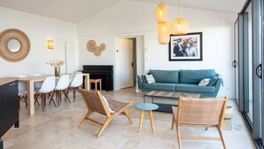 A spacious living room with a teal sofa, wicker chairs, a piano, and a dining area with white chairs and a wooden table. - Alma - Renovated villa with heated pool few blocks from the beach (LE BOIS PLAGE EN RE)
