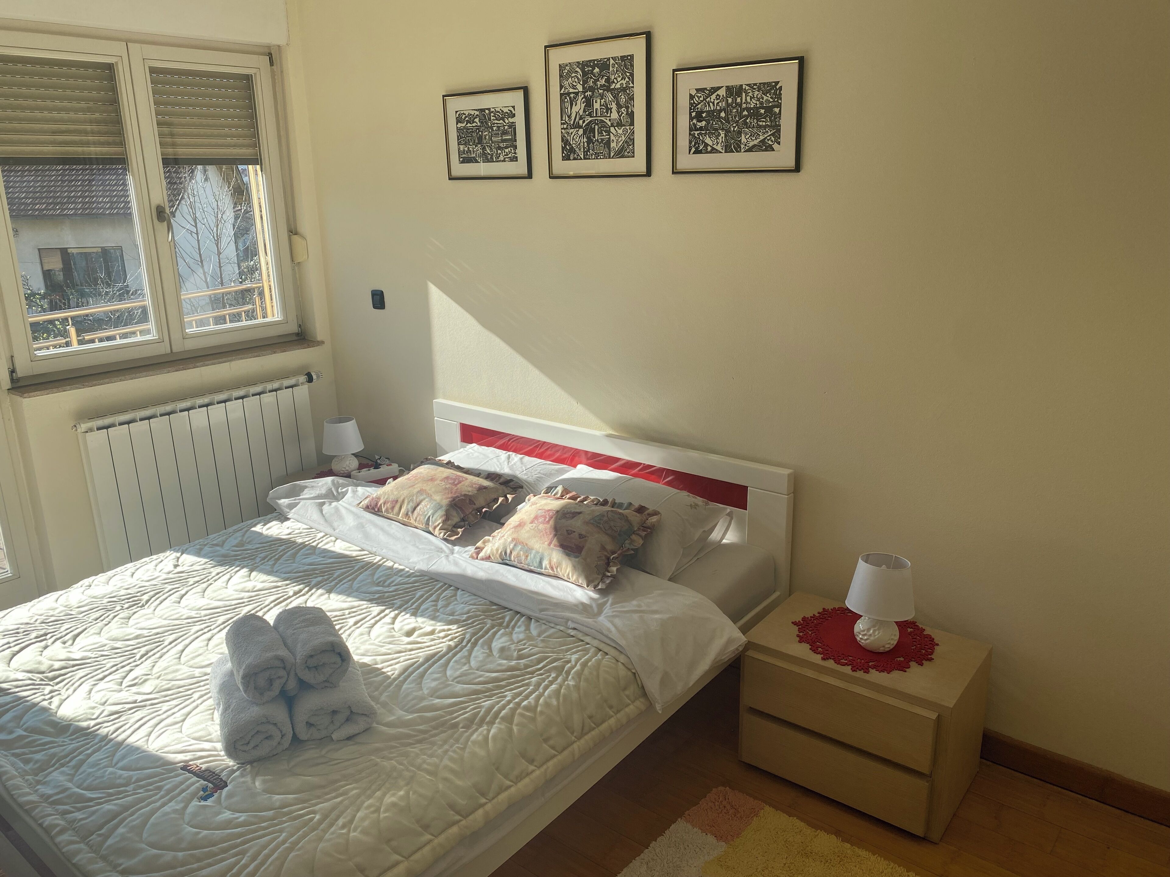 Un lit bien fait, avec des oreillers et une serviette enroulée, une table de chevet avec une lampe, et trois œuvres d’art encadrées accrochées au mur.