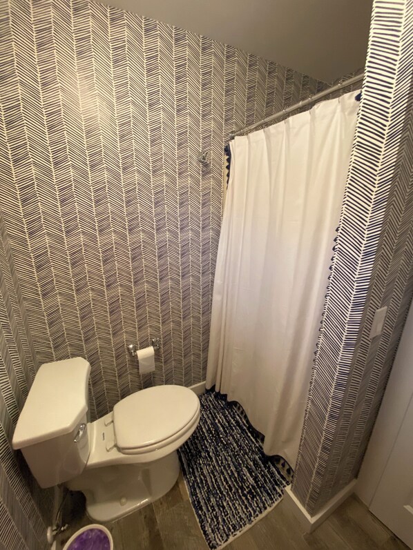 Un baño con pared estampada, inodoro blanco, cortina de ducha y alfombra.