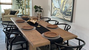 Un comedor con una mesa de madera larga, sillas negras, individuales tejidas y un cuadro abstracto grande en la pared.