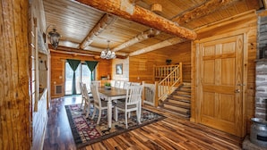 Interior de una cabaña de madera con comedor, escalera y chimenea.