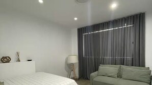 A modern bedroom with a bed, a green sofa, a patterned rug, and a large window with curtains. - Sanctuary on the Creek (Sanctuary Point)