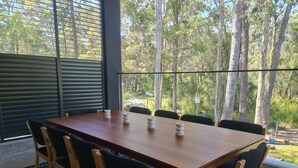 A wooden dining table with black chairs, set against a backdrop of trees and a view of the outdoors. - Sanctuary on the Creek (Sanctuary Point)