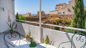 Un balcon avec une table et des chaises, des plantes en pot et une vue sur des bâtiments et des collines.