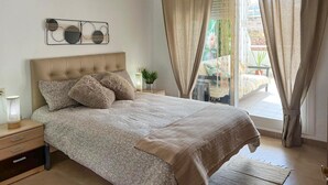 Une chambre à coucher comprenant un lit, une table de chevet, une lampe, une fenêtre avec des rideaux et une vue sur l’extérieur.