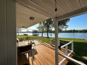 Une terrasse couverte avec vue sur un lac, une table avec des chaises et une rambarde.
