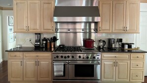 A kitchen with light wooden cabinets, a stainless steel range hood, a gas stove, and an oven.