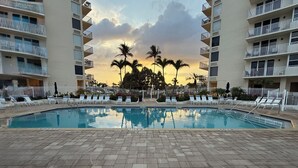 Zona de piscina con sillones de descanso y vistas a palmeras y un atardecer.