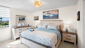 Un dormitorio con cama, mesitas de noche, cómoda y obras de arte en las paredes.