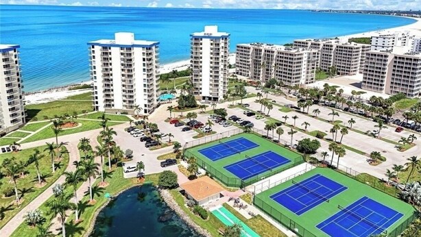 A high-rise hotel with multiple floors, a beach view, tennis courts, and a swimming pool.