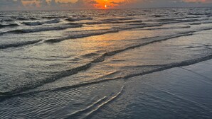 Una spiaggia con onde e un tramonto all'orizzonte.