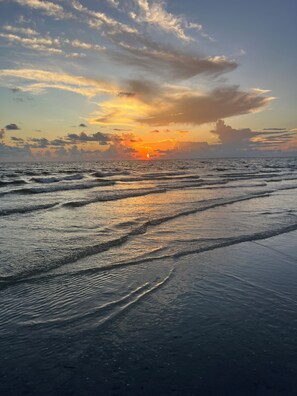 Una playa con olas y un atardecer a lo lejos.