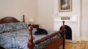 A bedroom with a large bed, a nightstand, a lamp, and a fireplace. - Country Style Louisa - Gawler  (Gawler)