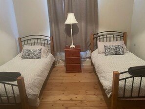 Two single beds with zebra-patterned pillows and white blankets, a wooden dresser, and a white lamp.