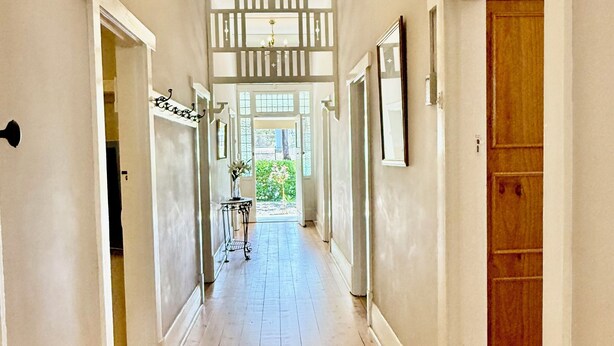 A hallway with wooden flooring, white walls, and a chandelier. There are doors on both sides and a window at the end. - Country Style Louisa - Gawler  (Gawler)