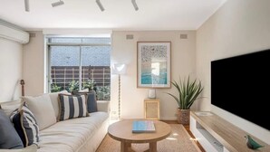 A modern living room with a sofa, a round coffee table, a flat-screen TV, a large window, and a framed artwork. - Luxe-Coastal Balmoral Townhouse
 (Mosman)