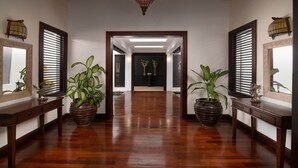 A hallway with wooden flooring, flanked by two large potted plants and two wall-mounted mirrors.