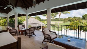 A covered outdoor seating area with wicker furniture, a pool, and a view of a golf course.