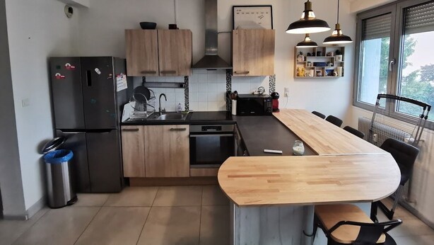 Eine moderne Küche mit Holzausstattung, einem schwarzen Kühlschrank, einem eingebauten Ofen und einer großen Kochinsel mit Holzarbeitsplatte.