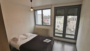 Ein Schlafzimmer mit einem Bett, einem Heizkörper, einem Fenster mit Jalousien und einer Pendelleuchte.