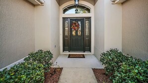 A house entrance with a dark door, a welcome mat, and two bushes on either side.