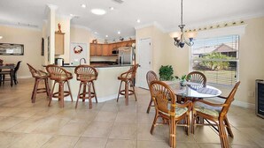 A spacious kitchen with a central island, dining area with wicker chairs, and a view of the outdoors.
