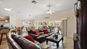 A spacious living room with leather sofas, a dining area with wicker chairs, and a kitchen in the background.