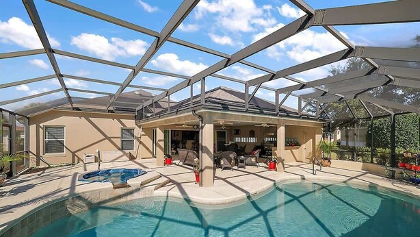A covered swimming pool with a glass ceiling, lounge chairs, and a patio area.