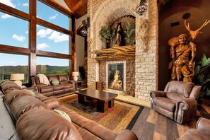 A spacious living room with a stone fireplace, leather furniture, and a large window offering a view of the outdoors.