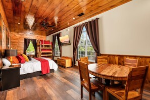 A cabin interior with a wooden ceiling, a bunk bed, a dining table with chairs, and a television mounted on the wall. - Excalibur: Pickleball, Duck Pin Bowling, Indoor Pool, 9 Hole Golf (Sevierville)