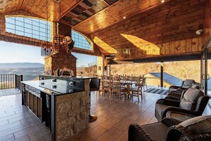 A spacious outdoor area with a stone fireplace, wooden dining table, and comfortable seating.