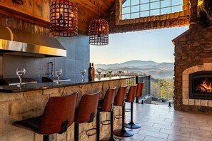 A bar area with a stone counter, bar stools, hanging lights, and a fireplace.