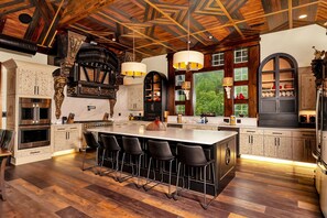 A spacious kitchen with a large island, bar stools, and a view of the outdoors through large windows. - Excalibur: Pickleball, Duck Pin Bowling, Indoor Pool, 9 Hole Golf (Sevierville)