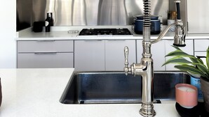 Une cuisine moderne dotée d’une hotte en acier inoxydable, d’un four encastré, d’une cuisinière à gaz et d’un évier avec un robinet à tuyau flexible.