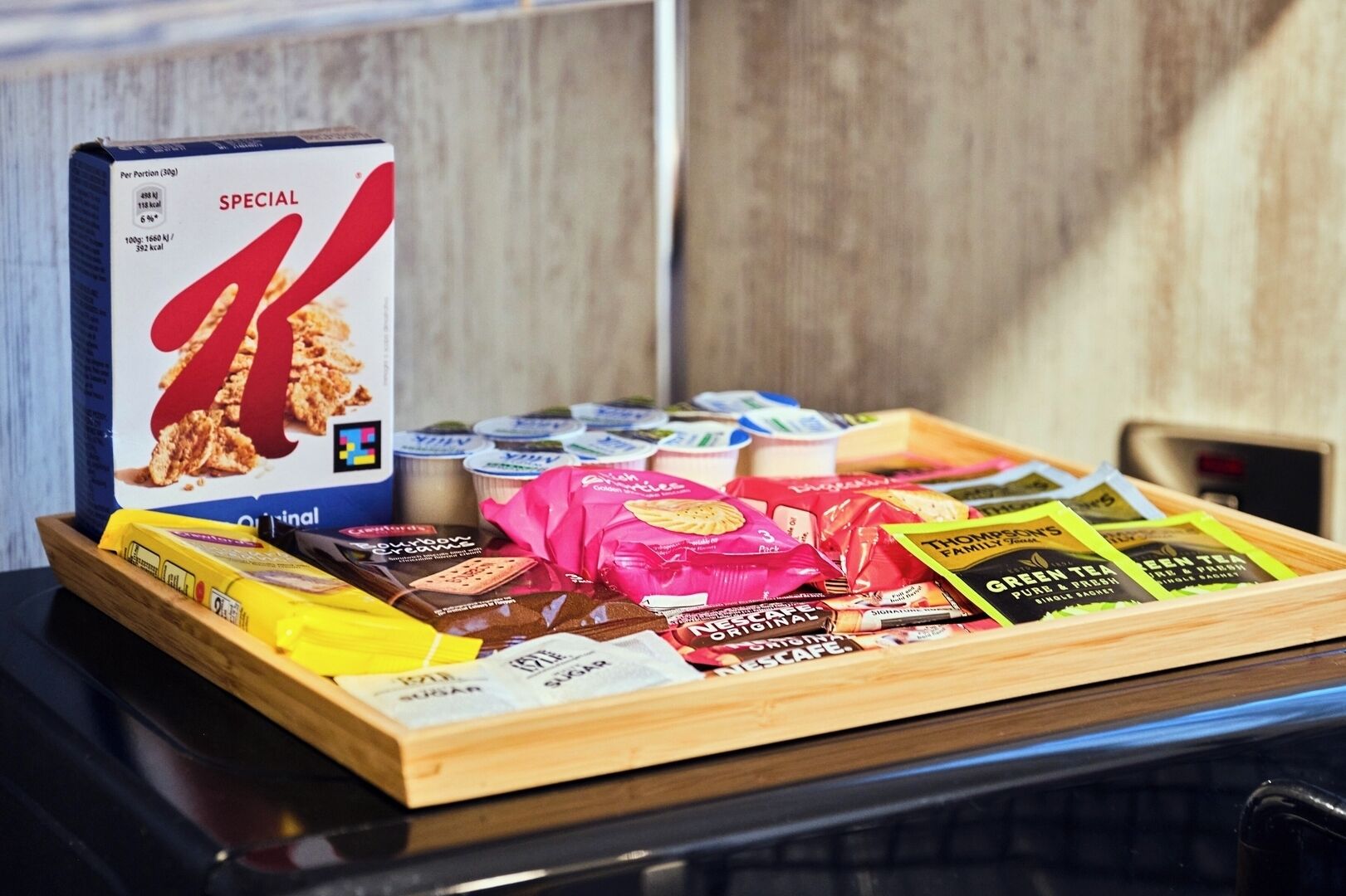 Een schaal met diverse snacks, waaronder ontbijtgranen, chocolade en theezakjes.