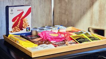 Een schaal met diverse snacks, waaronder ontbijtgranen, chocolade en theezakjes.