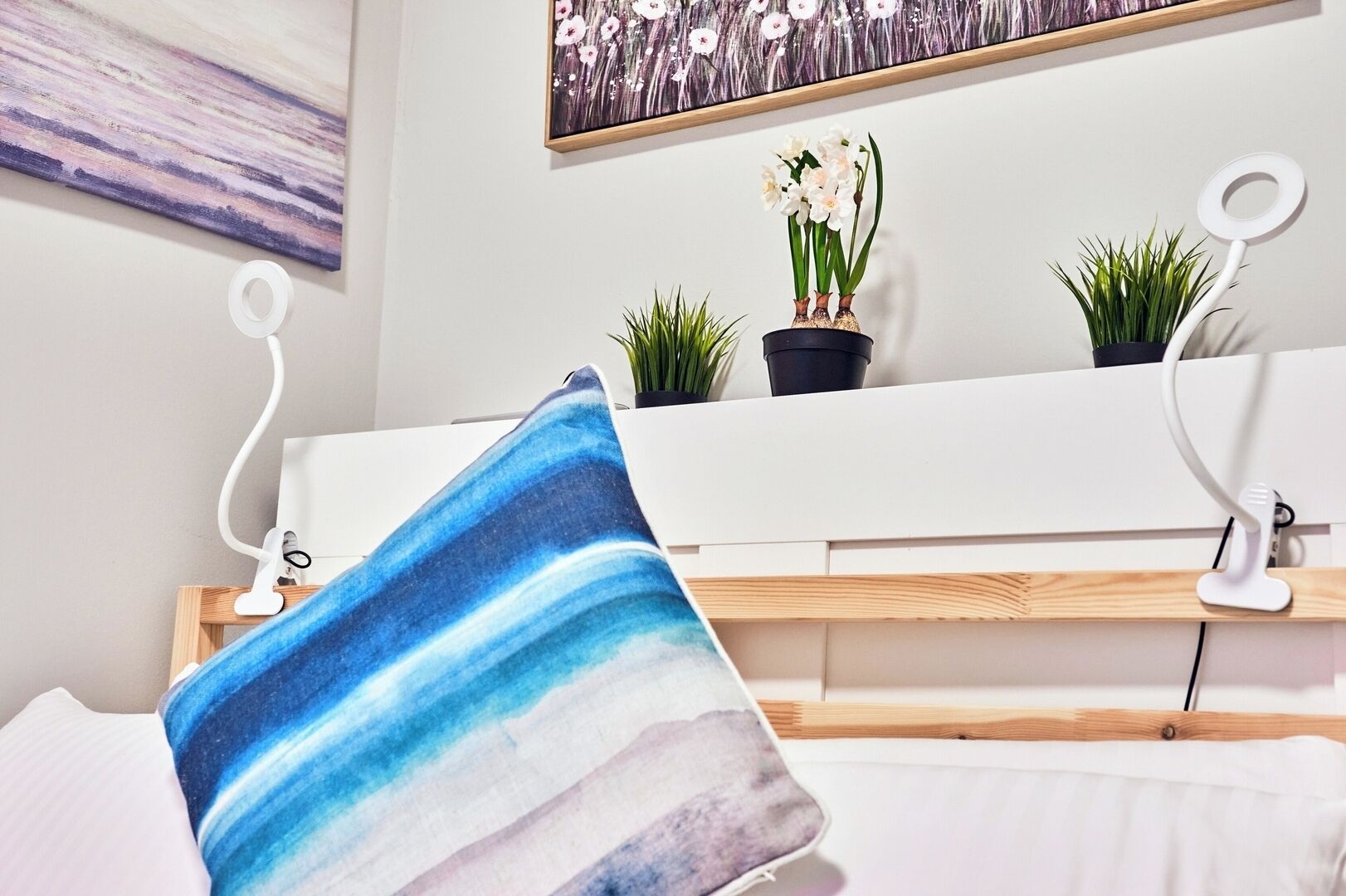 Ein ordentlich eingerichtetes Schlafzimmer mit einem Bett, einem Nachttisch, einer Wandablage mit Topfpflanzen und einem Gemälde darüber.