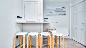 Een moderne keuken met witte kastjes, een wit aanrecht en vier houten barkrukken.