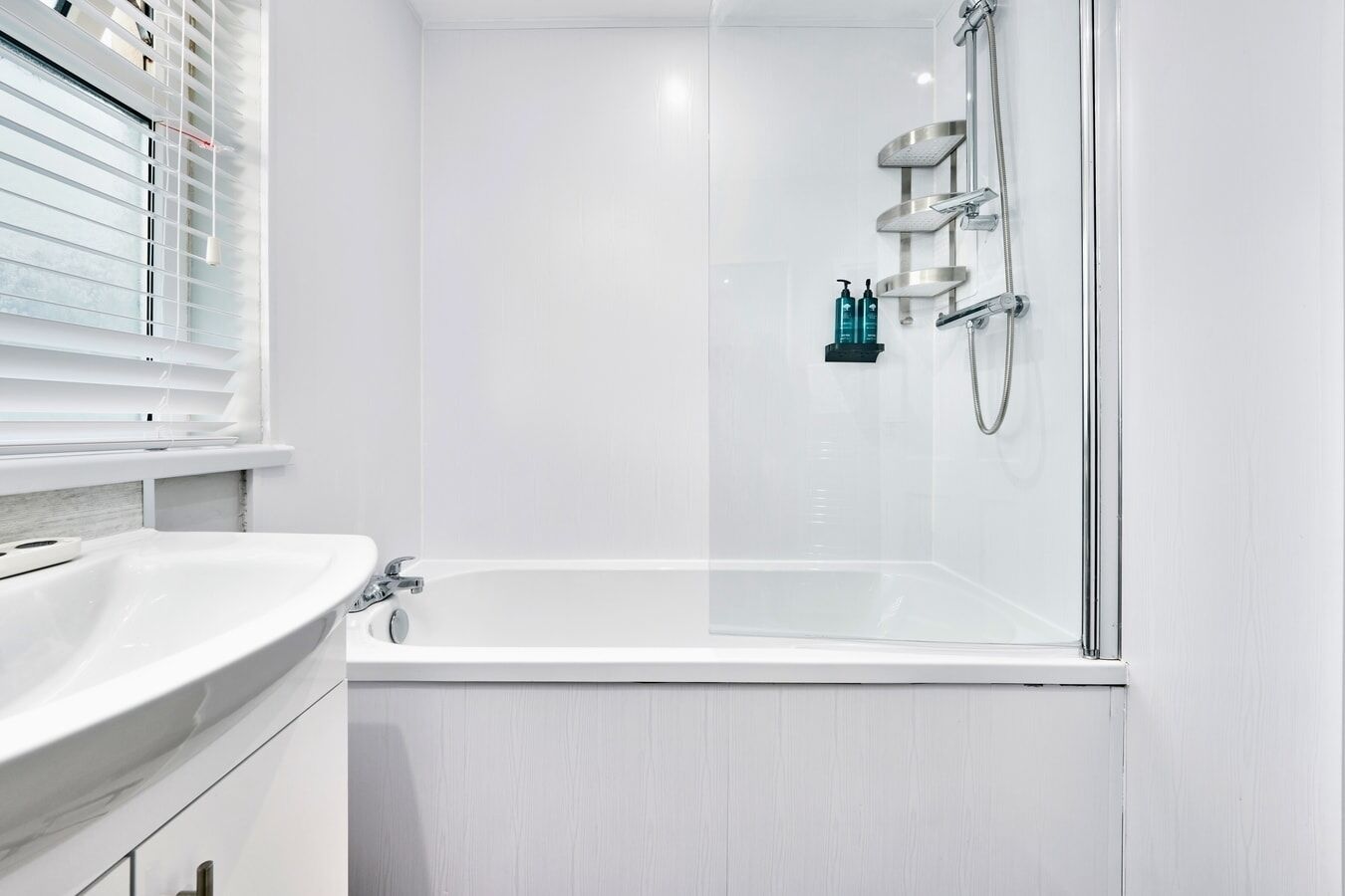 A modern bathroom with a white bathtub, a glass-enclosed shower, and a window with blinds.