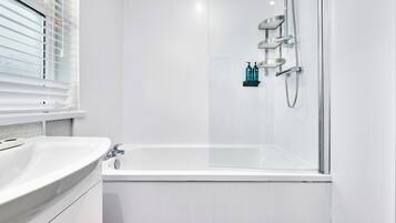 A modern bathroom with a white bathtub, a glass-enclosed shower, and a window with blinds.